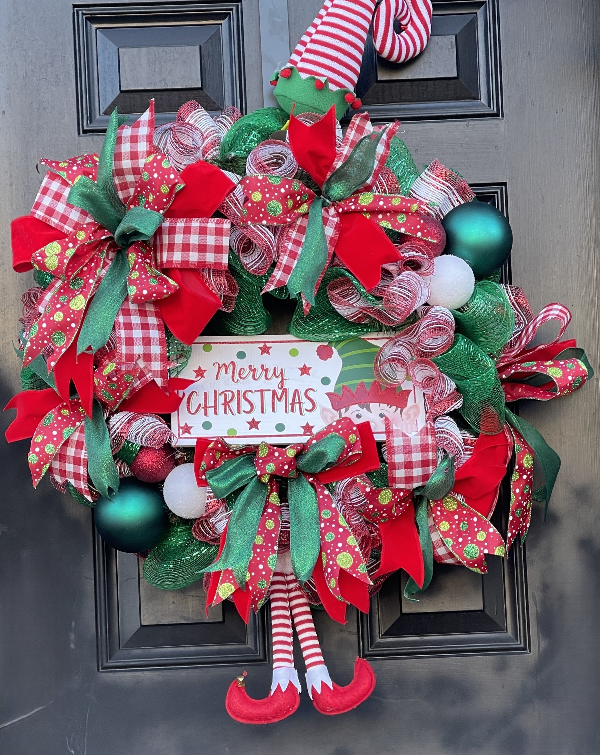 Celebrate the season with this whimsical Christmas wreath, bursting with festive flair! Designed with vibrant red, green, and white ribbons—including gingham, glitter, and polka dots—this wreath features playful mesh accents, colorful ornaments, and a cheerful “Merry Christmas” sign. Below the centerpiece, a pair of elf legs with striped stockings and red shoes add a joyful, storybook touch. Perfect for front doors, mantels, or gifting, this wreath brings laughter and holiday magic to any space.
MPN: GO-XMA